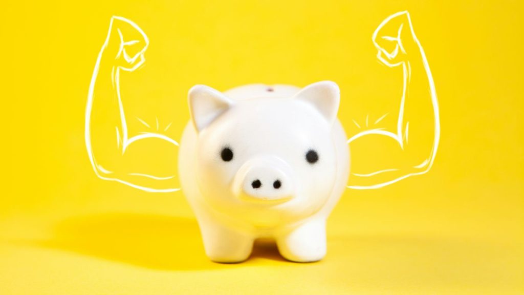 A white piggy bank with drawn muscular arms.