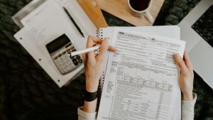 Person reviewing documents with calculator and laptop.