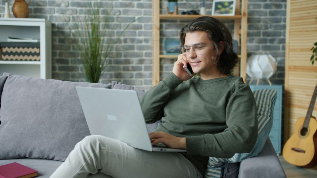 Man talking on phone while using laptop on couch