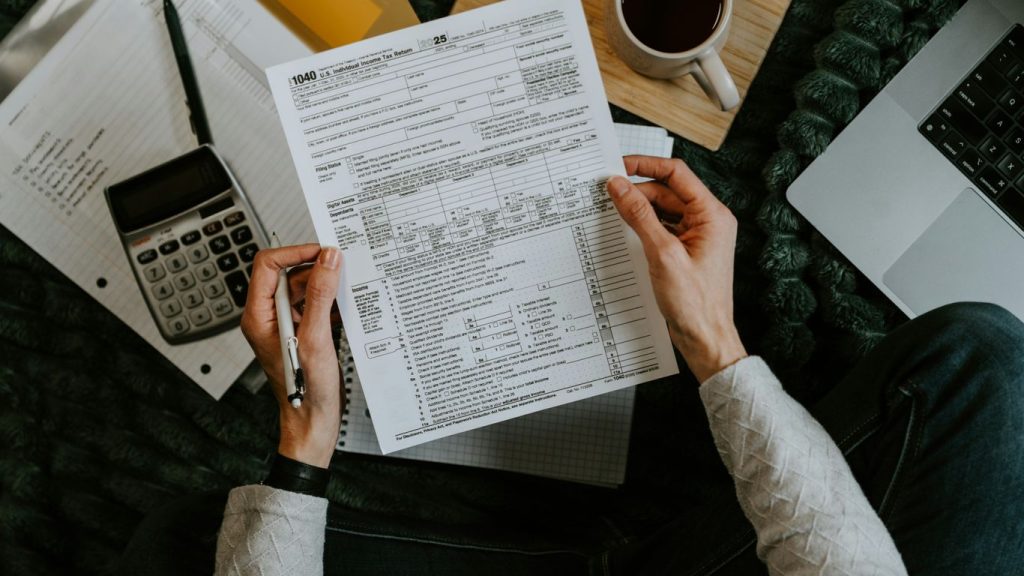 Hands holding tax forms with calculator and laptop.