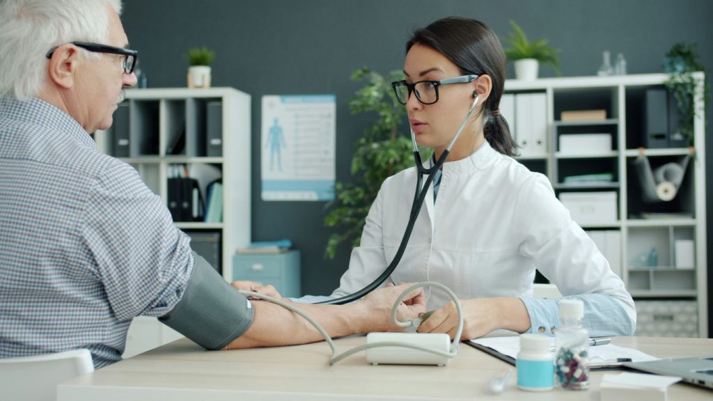 Doctor takes elderly patient's blood pressure.