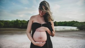 Pregnant woman in black dress touching her belly