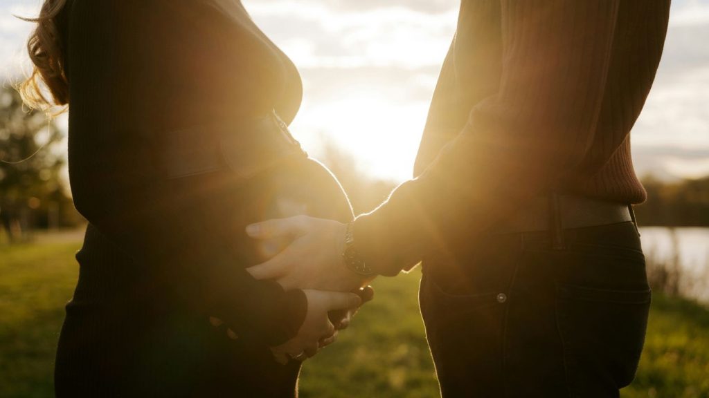 Couple holding pregnant belly at sunset