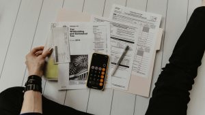 person holding paper near pen and calculator