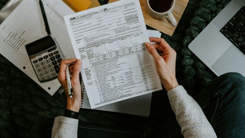 Hands holding tax forms with calculator and laptop.